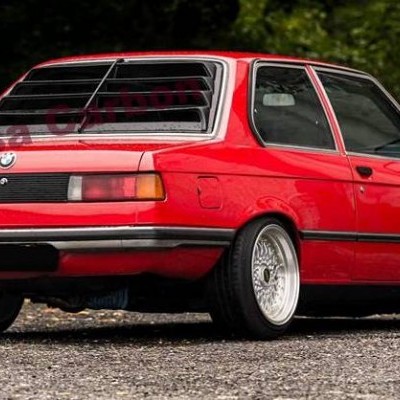 Carro clássico BMW vermelho com jantes brancas e persianas pretas nas janelas traseiras