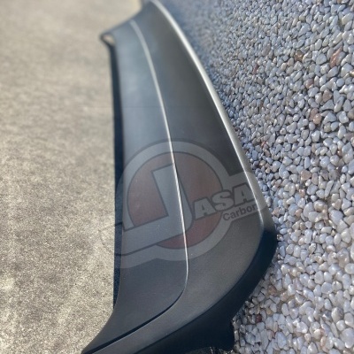 Spoiler de automóvel preto encostado numa parede texturada de seixos