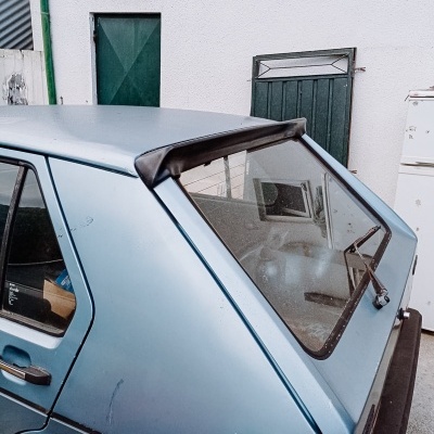 Traseira de carro azul claro com detalhes pretos junto a parede branca e portas verdes