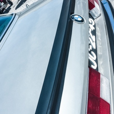 Detalhe traseiro de carro BMW prata com spoiler preto e motocicleta ao fundo