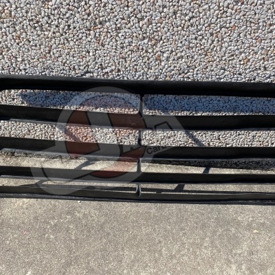 Grelha automóvel preta com várias barras horizontais encostada a uma parede de pedras claras.