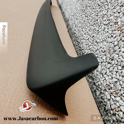 Spoiler traseiro preto fosco em superfície castanha ao lado de pedras cinzentas