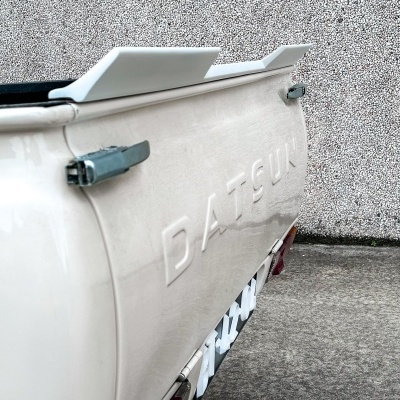 Parte traseira branca de carrinha pick-up Datsun com letras em relevo e fechaduras azuis