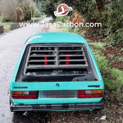 Carro clássico azul claro com grelha preta na janela traseira numa estrada envolta por vegetação