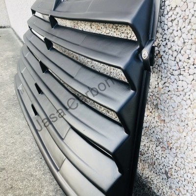 Grelha preta de carro com lâminas horizontais encostada numa parede de pedra branca