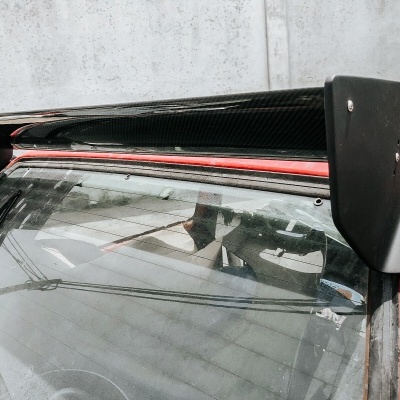 Asa traseira preta em fibra de carbono montada num carro vermelho