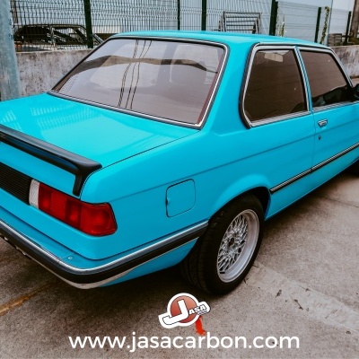 Carro BMW clássico azul celeste com spoiler preto estacionado em parque de cimento
