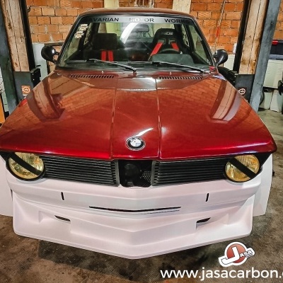 Automóvel BMW clássico vermelho e branco em garagem com tijolos
