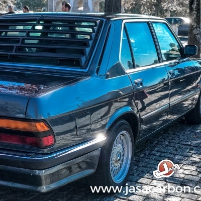 Carro sedan azul clássico estacionado num passeio de pedra em área urbana