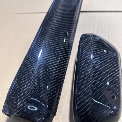 Peças fabricadas em carbono brilhante com padrão entrelaçado preto, sobre superfície clara