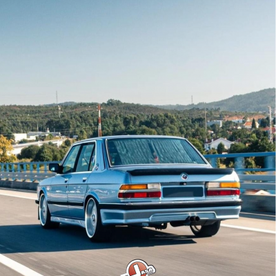 Carro clássico azul traseira em estrada com morros e árvores ao fundo