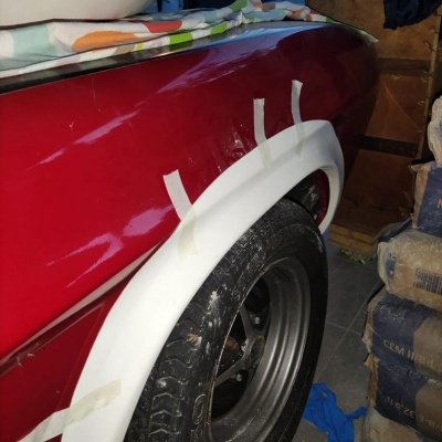 Parte traseira lateral de carro vermelho com guarda-lamas branco e pneu preto num espaço interior