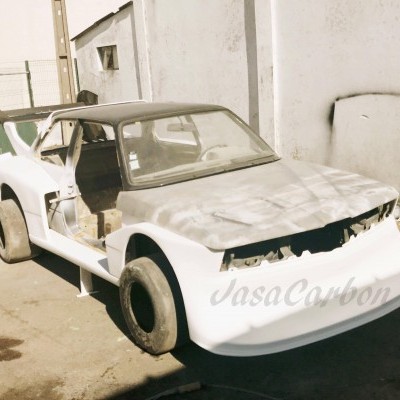 Carro de corridas branco em construção num pátio junto a paredes brancas.
