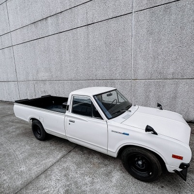 Carrinha pick-up branca com texto DATSUN 1200 na lateral, em fundo cinzento