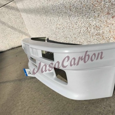 Para-choques frontal de carro branco com inscrição JasaCarbon em vermelho claro no chão junto a parede de estuque