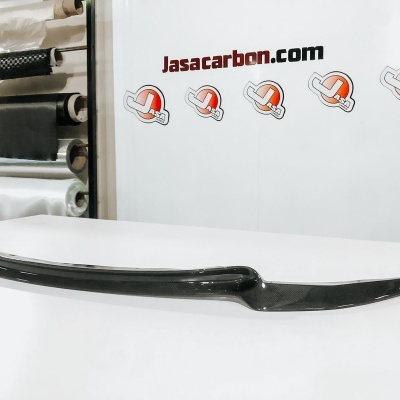 Barra de fibra de carbono preta brilhante sobre mesa branca com parede e texto Jasacarbon.com ao fundo