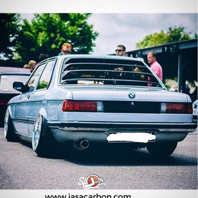 BMW cinzento claro visto de trás com jantes largas e suspensão baixa em encontro automóvel