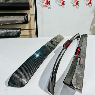 Peças de fibra de carbono sobre mesa branca com rolos ao fundo e cartaz Jasarcarbon.com