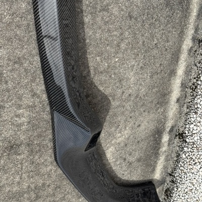 Defletor aerodinâmico em fibra de carbono preta sobre chão cinzento com cascalho