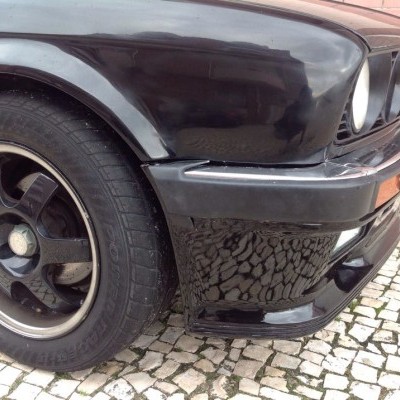 Parte dianteira de carro clássico preto com roda preta e piso de calçada portuguesa