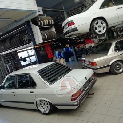 Três carros BMW E28 brancos em garagem com pneus e iluminação natural