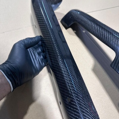 Peças automotivas em fibra de carbono com padrão de trama visível sobre superfície clara