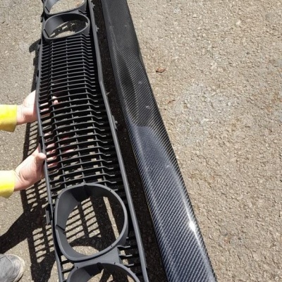 Peças automóvel preto e fibra de carbono sobre chão de terra.