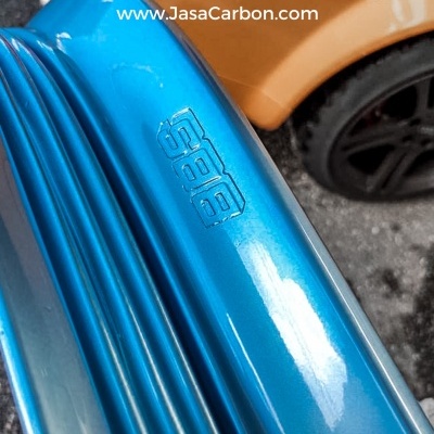 Spoiler azul metálico com logotipo SAB e carro laranja ao fundo