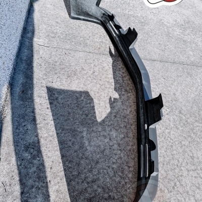 Peça automóvel preto e cinzento em material de carbono ou plástico sobre piso de cimento