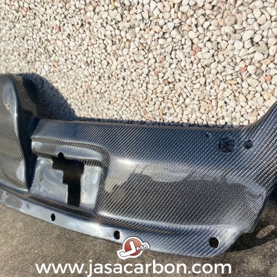 Parachoques automático em fibra de carbono preto com padrão quadriculado encostado numa parede de pedras pequenas claras.