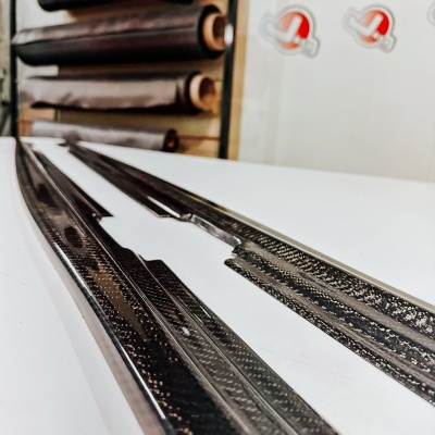 Duas lâminas metálicas texturizadas sobre superfície branca, rolos ao fundo, parede com texto