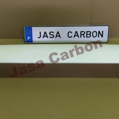 Spoiler traseiro branco com texto JASA CARBON numa placa atrás, colocado sobre superfície castanha