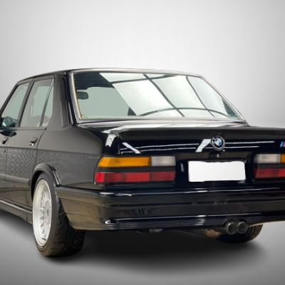 Carro BMW M3 E30 preto visto de trás com jantes prateadas e escape duplo