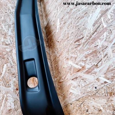 Peça automóvel preta sobre superfície de madeira prensada com texto www.jasaecarbon.com e logótipo JASA