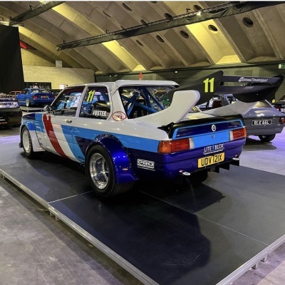 Carro de corrida BMW azul, branca e vermelha com asa traseira e matrícula inglesa