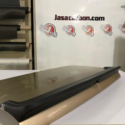 Porta-malas ou spoiler cinza com bordas pretas sobre superfície branca com fundo escrito Jasacarbon.com