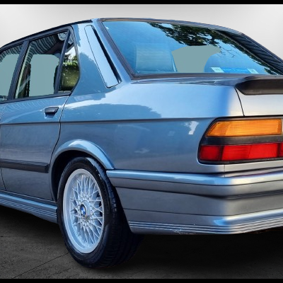 BMW E30 azul claro metálico visto de trás e lado com jantes brancas