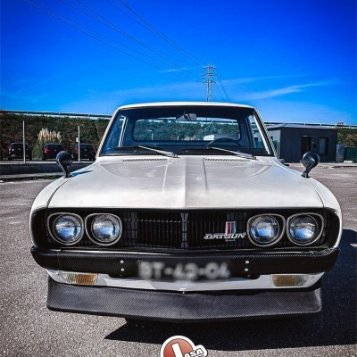 Carro clássico Datsun branco visto de frente com faróis duplos e grelha preta