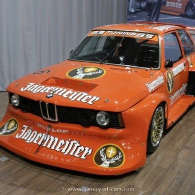 Carro de corrida BMW laranja com logótipo Jägermeister exposto em interior.