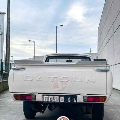 Traseira de carrinha pick-up Datsun branca com letras DATSUN em relevo na tampa da caçamba.
