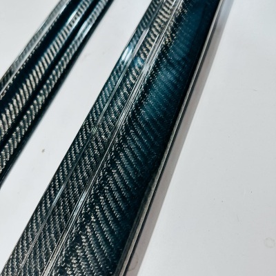 Duas réguas de fibra de carbono preta e cinza com padrão entrelaçado sobre superfície branca