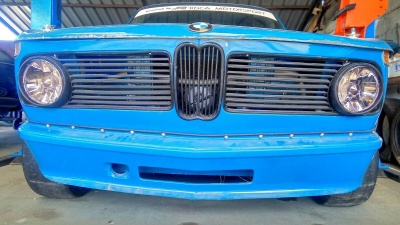 Frente de carro clássico azul com faróis circulares e grelha preta em oficina