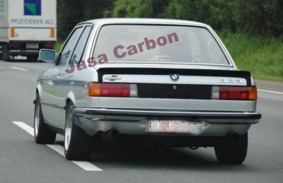 Carro BMW 323i prata visto de trás numa estrada com texto Jasa Carbon