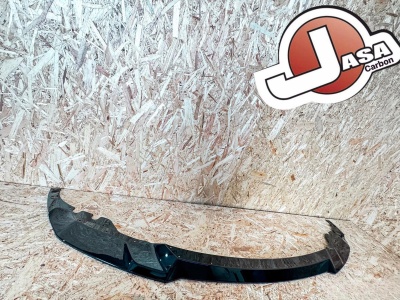 Peça automóvel preta com autocolante JASA Carbon contra parede de madeira