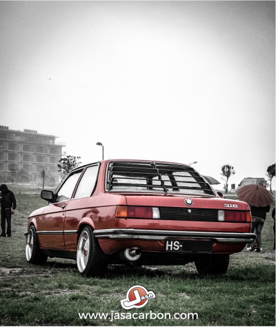 BMW 316 vermelho metalizado estacionado em relva com persiana traseira preta