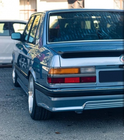Carro cinzento metálico visto de trás com faróis traseiros e jantes prata.