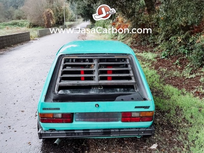 Carro clássico azul claro com grelha preta na janela traseira numa estrada envolta por vegetação