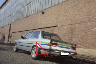 Automóvel cinzento com faixas coloridas estacionado junto a uma parede de tijolos