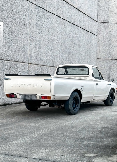 Carrinha pick-up Datsun branca estacionada junto a paredes cinzentas de betão