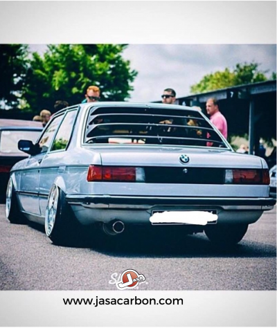 BMW cinzento claro visto de trás com jantes largas e suspensão baixa em encontro automóvel